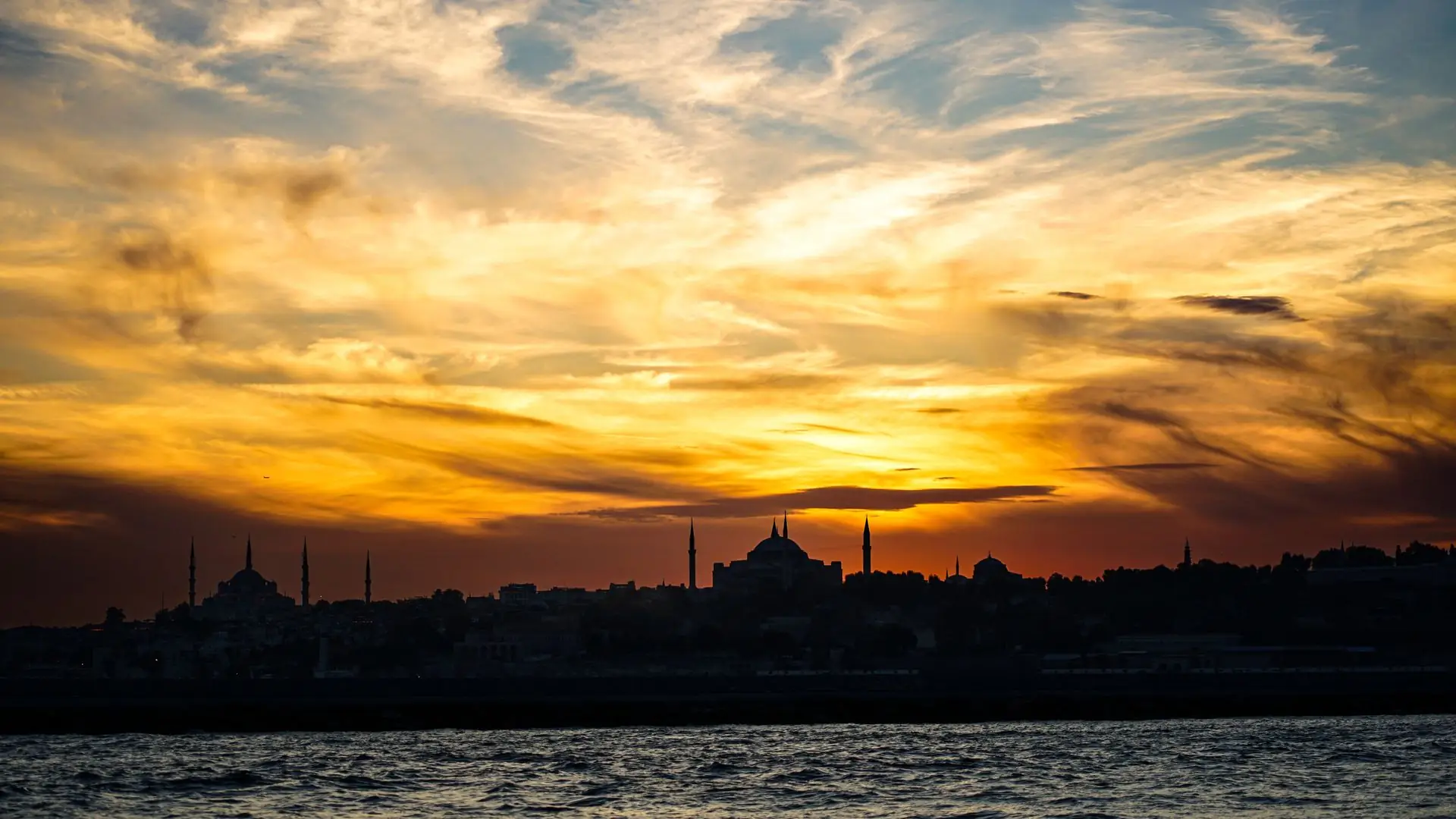 The minarets and domes of Hagia Sophia and the Blue Mosque silhouetted at sunset over the water