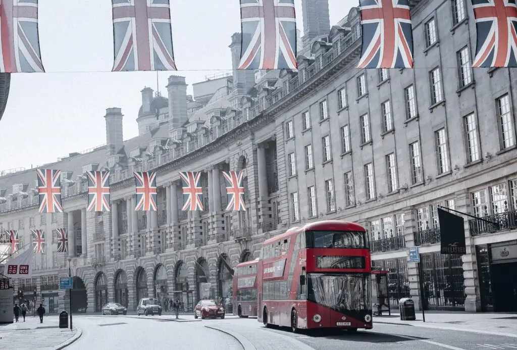 A red double-decker bus on Regent Street in London with Union Jack flags above