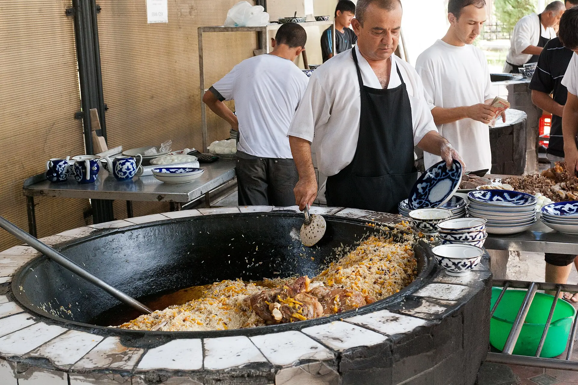 Cook serving plov from a giant kazan with a long skimmer in Tashkent