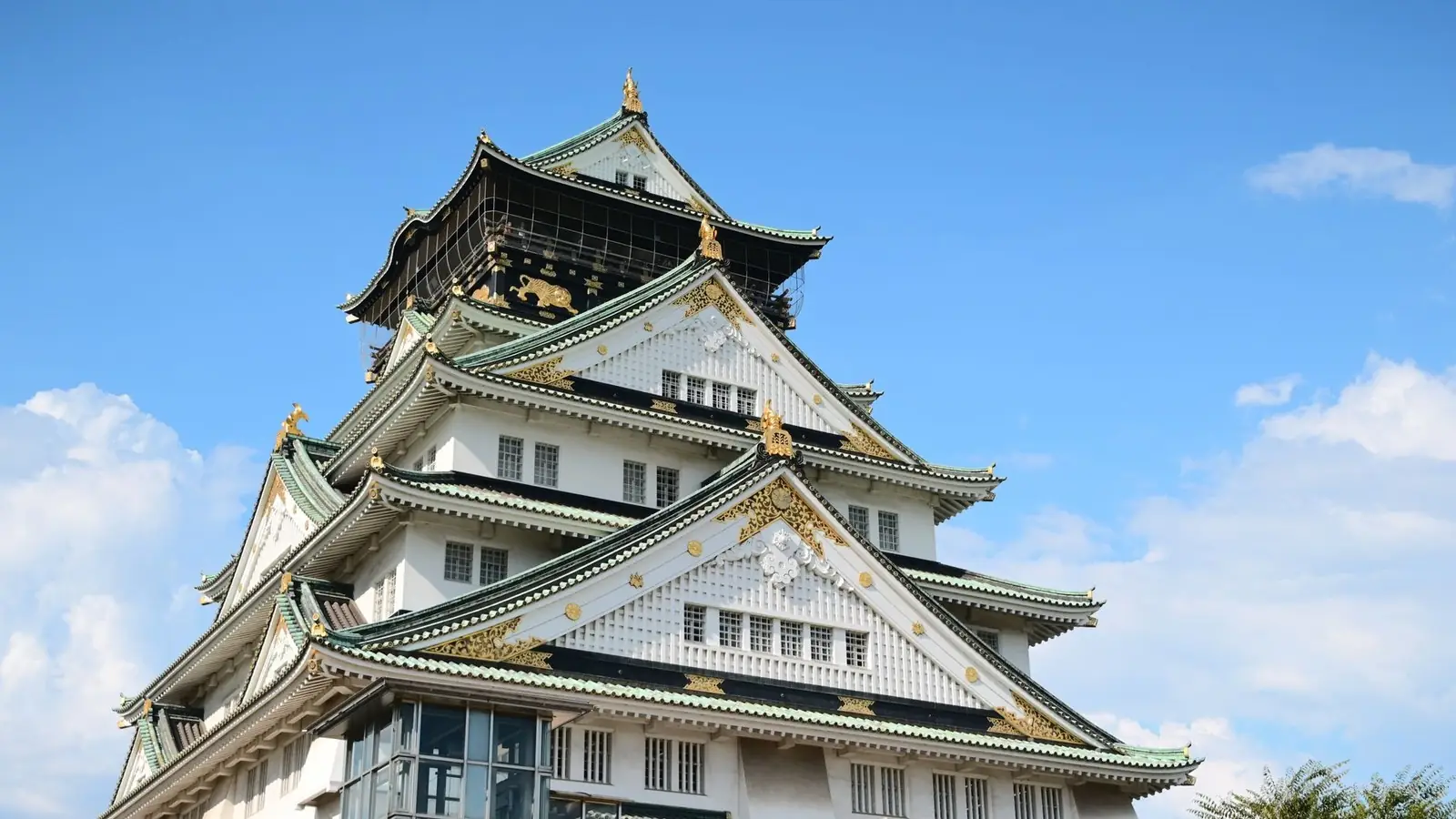 Osaka Castle with its white walls, green roofs and gold trim against a blue sky
