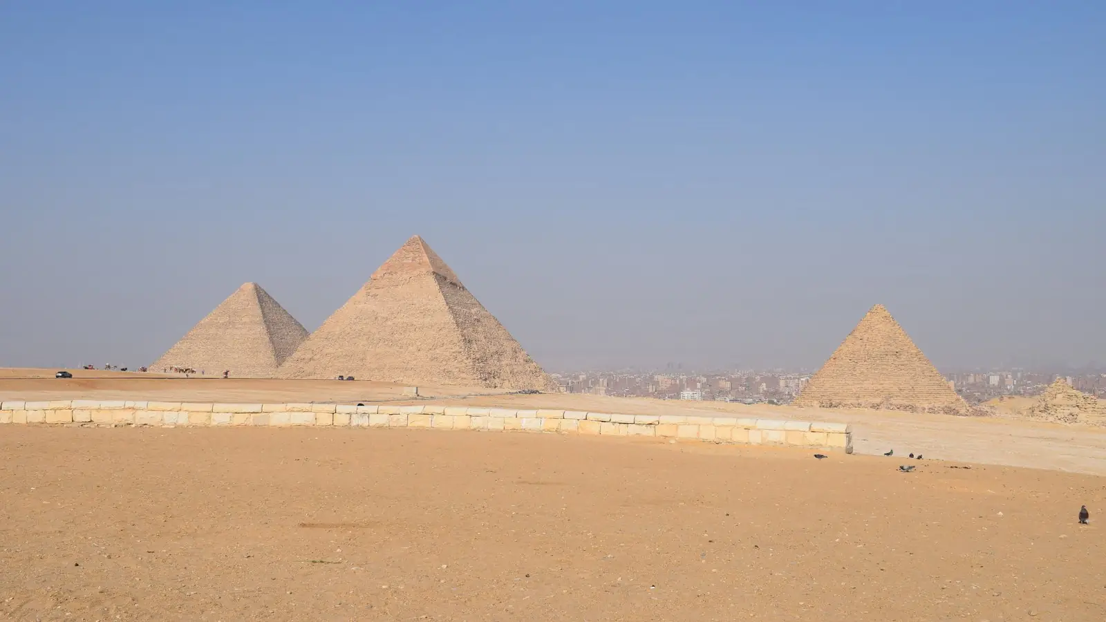The pyramids of Giza under a clear blue sky with the edge of Cairo visible behind