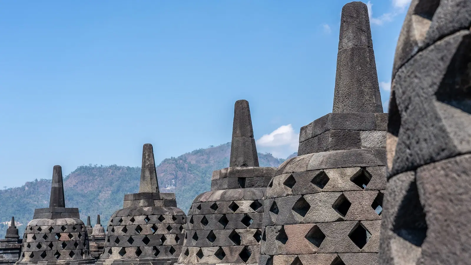 Latticed stone stupas on the upper terraces of Borobudur with green hills behind